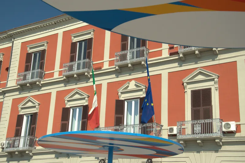 Un palais avec des drapeaux et des parasols colorés au premier plan, Tarente