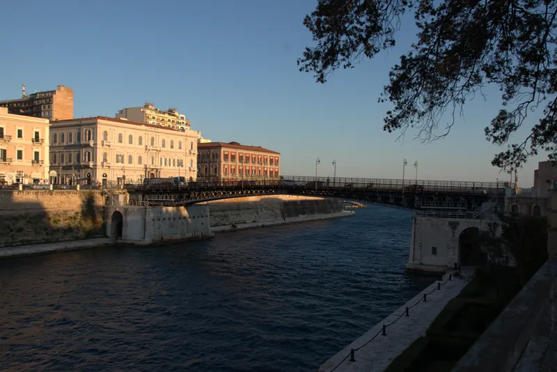 Il canale navigabile di Taranto incorniciato dagli alberi, con Palazzo degli Uffici
